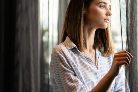 Fiatal nő néz ki az ablakon reggeli fényben