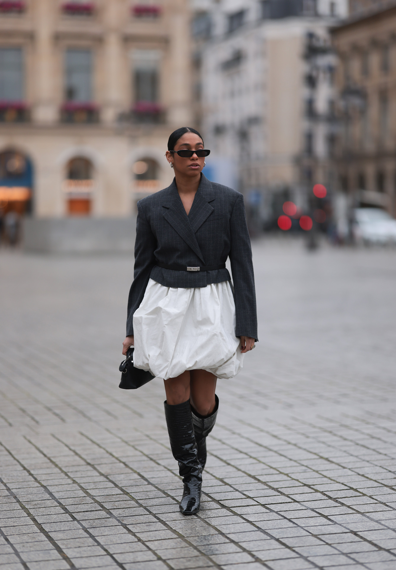 Fekete blézert, fehér szoknyát és cowboy csizmát viselő napszemüveges nő