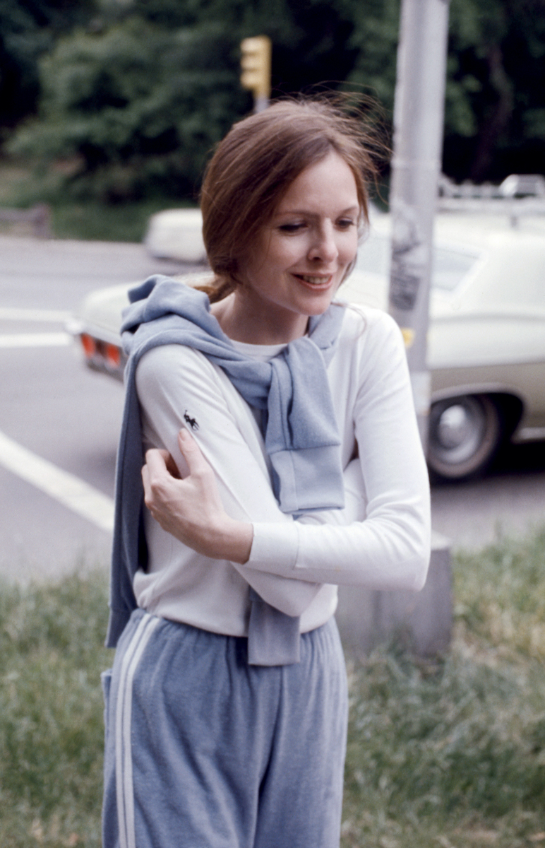 Diane Keaton 1975-ben, az utcán sétál mosolyogva, karját maga előtt keresztezi, fehér felsőben és kék nadrágban, vállán pulóver van átvetve