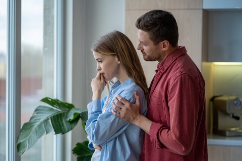 Férfi áll a szomorú nő háta mögött