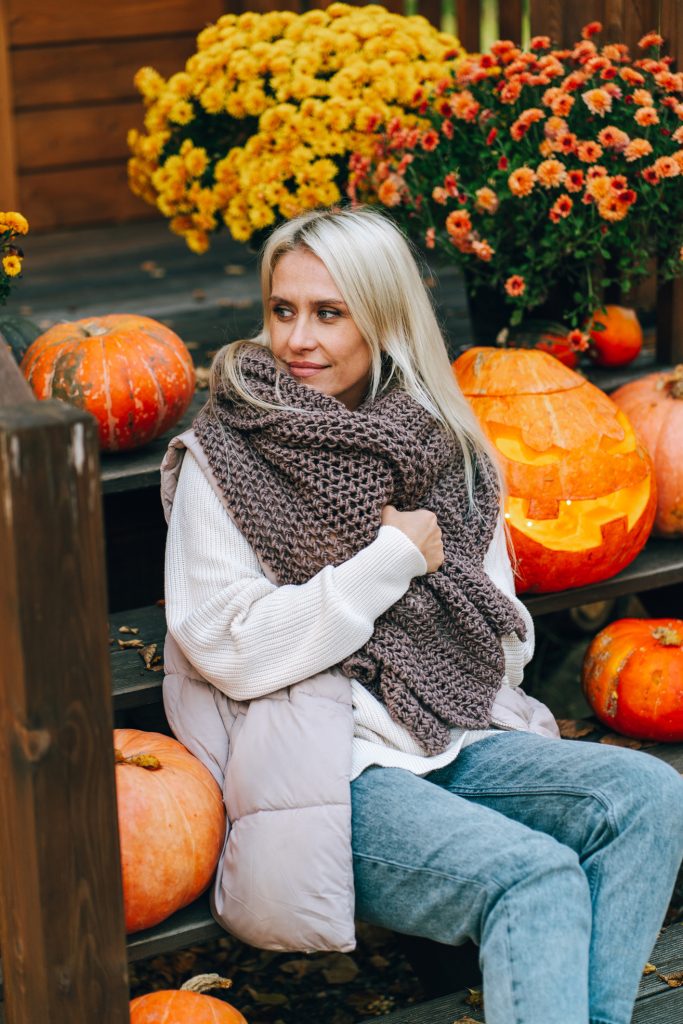 Egy nő élvezi az őszi hangulatot a verandán tökökkel és virágokkal