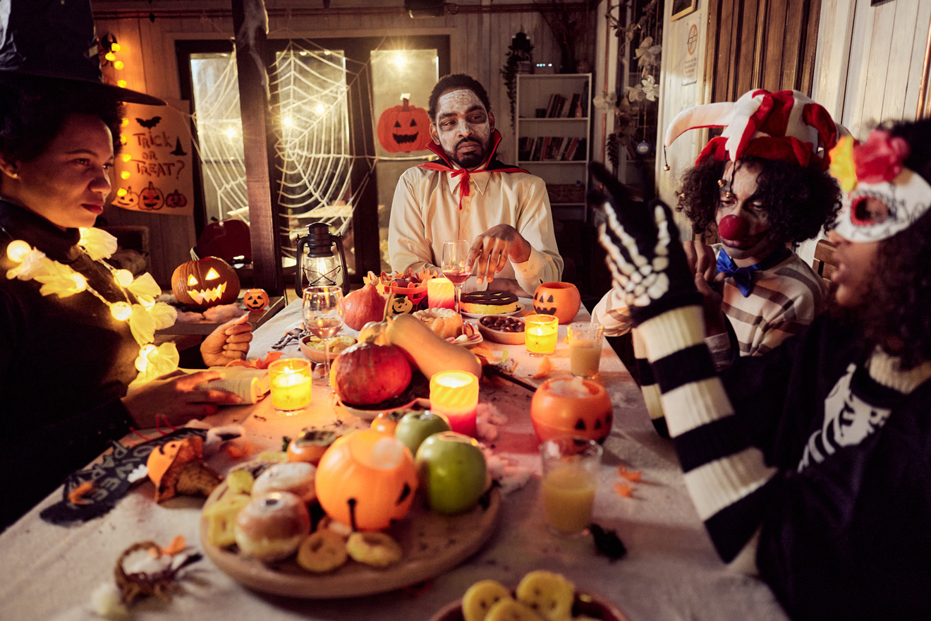 Jelmezeket viselő afroamerikai család ünnepli a halloweent este az étkezőasztalnál