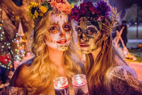 Dia de los Muertos – mexikói ünnep, két nő gyertyát tart a kezében, élénk arcfestéssel és virágkoszorúval a fejükön