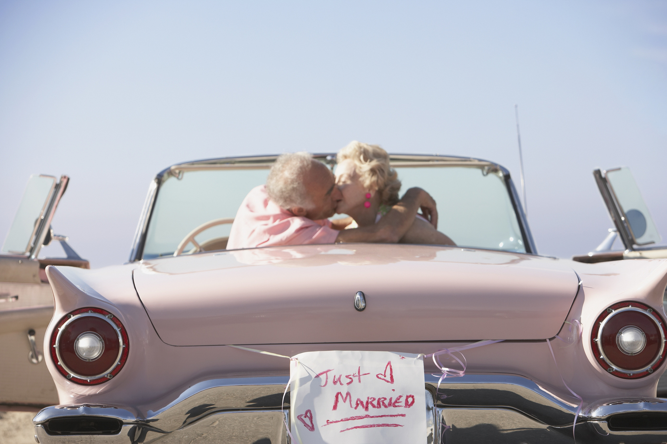 Idősebb pár autóban ülve csókolózik, épp összeházasodtak 