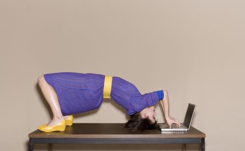 Hajlékony nő lila ruhában fejjel lefelé dolgozik a laptopján