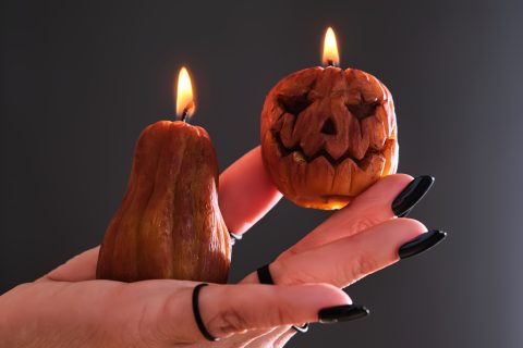 Női kéz fekete manikűrrel, gyűrűkkel, két kis tök alakú gyertyát tart – Halloween