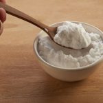 Fehér tálkából szódabikarbónát fa kanállal merítő kéz
