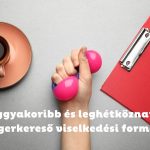 Szürke asztalon barna csészében kávé, kéz rózsaszín stresszlabdával, piros és zöld mappa