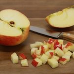 Alma félbe vágva fa asztalon, az egyik fél felkockázva, felgerezdelve, a kés mellette