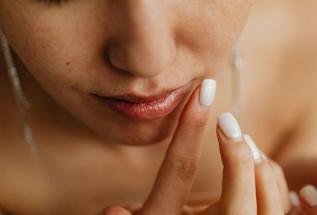 Fiatal nő fehérre lakkozott körömmel érinti meg érzékeny bőrét közeli képen