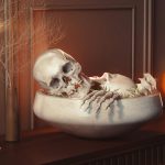 Halloween dekoráció gyertyákkal, világító tökkel és egy tálban csontvázdarabokkal, koponyával