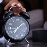 Fekete ébresztőórát lenyomó kéz kinyúl az ágyból