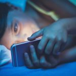 Ágyban telefonozó nő, az arcát megvilágítja a képernyő kék fénye