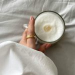 Nő, ujján aranygyűrűvel az ágyban cappuccinót fog