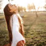 Hosszú, barna hajú nő fehér pulóverben élvezi az őszi napfényt