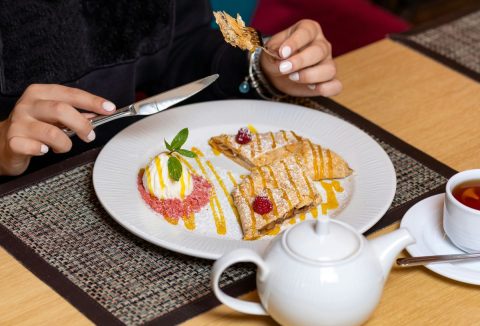 Fehérre lakkozott körmű nő késsel és villával rétest eszik