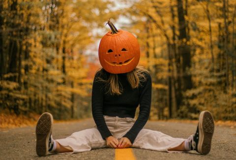 Nő erdei úton terpeszben ül, fején kifaragott halloween tökkel