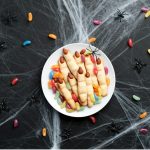 Klasszikus halloween sütemény, a boszorkányujj formájú keksz fehér tányéron jelly bean cukorkákkal körülötte és pókháló dekorációval