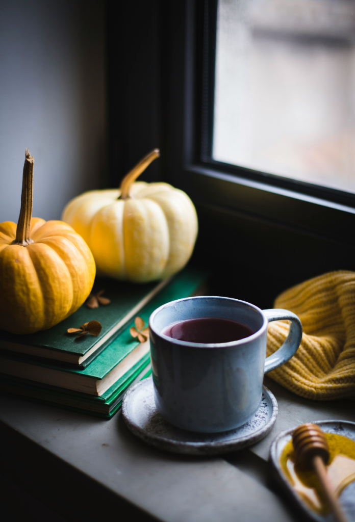 Őszi csendélet ablakban, két dísztökkel könyvekkel, egy csésze kávéval, sárga kötött sállal