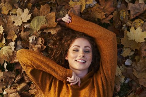 Mosolygós vörös hajú nő fekszik őszi leveleken a parkban