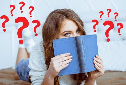 Szép fiatal, kék szemű nő az ágyon hasal, kék könyvet tart az arca elé, piros kérdőjelek