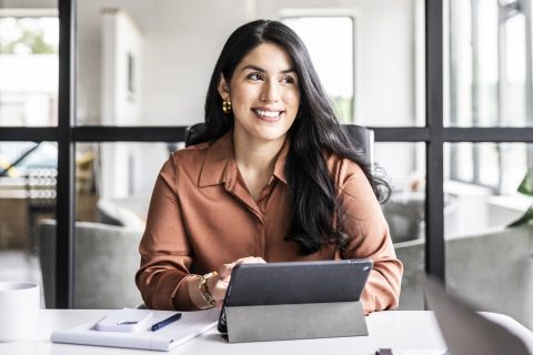 Egy barna inget viselő üzletasszony ül egy irodában, előtte tablet