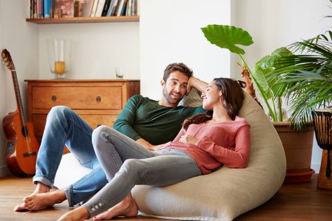 Mosolygós fiatal pár, akik otthon a babzsákkanapén beszélgetnek