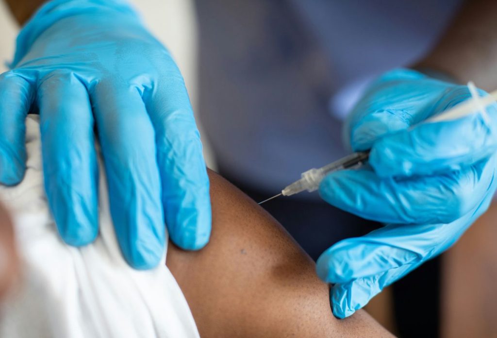 Kék gumikesztyűben oltást adnak vállba