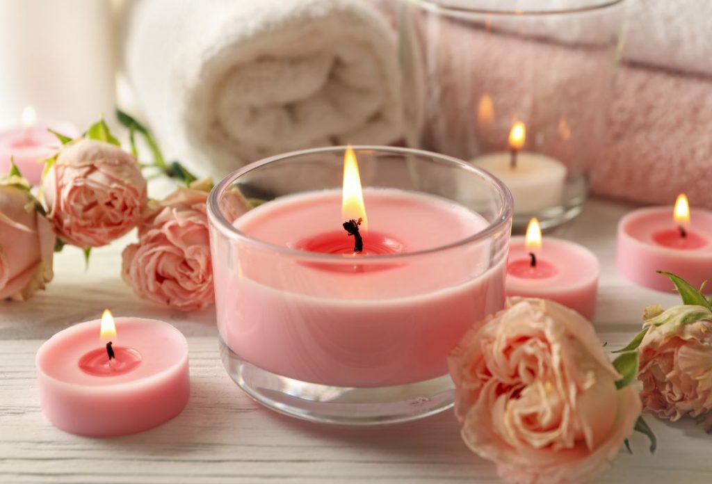 Rózsaszín illatgyertyák, kicsi és nagy, háttérben frottír törölköző feltekerve, halványrózsaszín rózsák