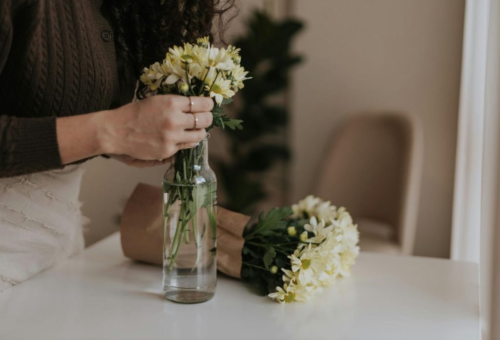 Nő apró fehér virágokat helyez átlátszó vázába