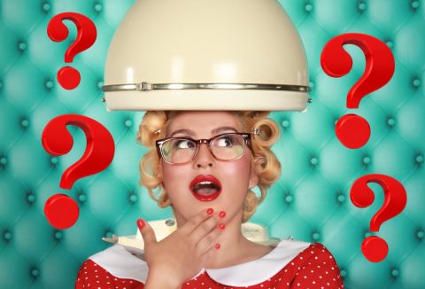 Retró stílusban, fehér körgalléros piros ruhában ül a búra alatt szemüveges, szőke nő és pirosra lakkozott körmű kezét a szája elé emeli, türkiz műbőr háttér előtt