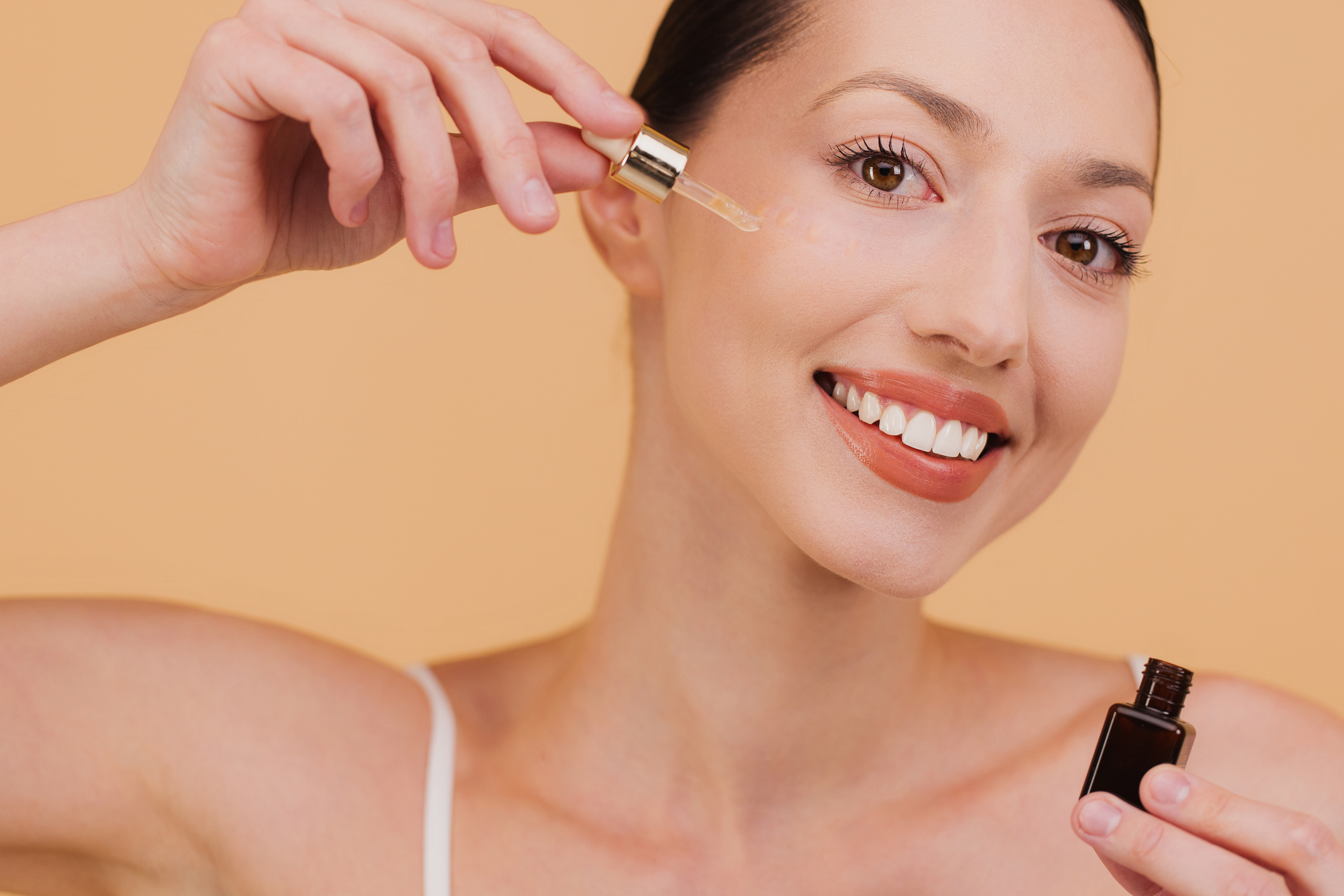 Szép, mosolygós nő szérummal keni az arcbőrét