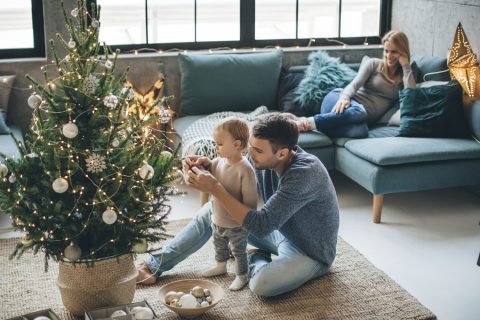 Egygyermekes család karácsonyfát díszít. Boldogok és élvezik az ünnepekre való készülődést.