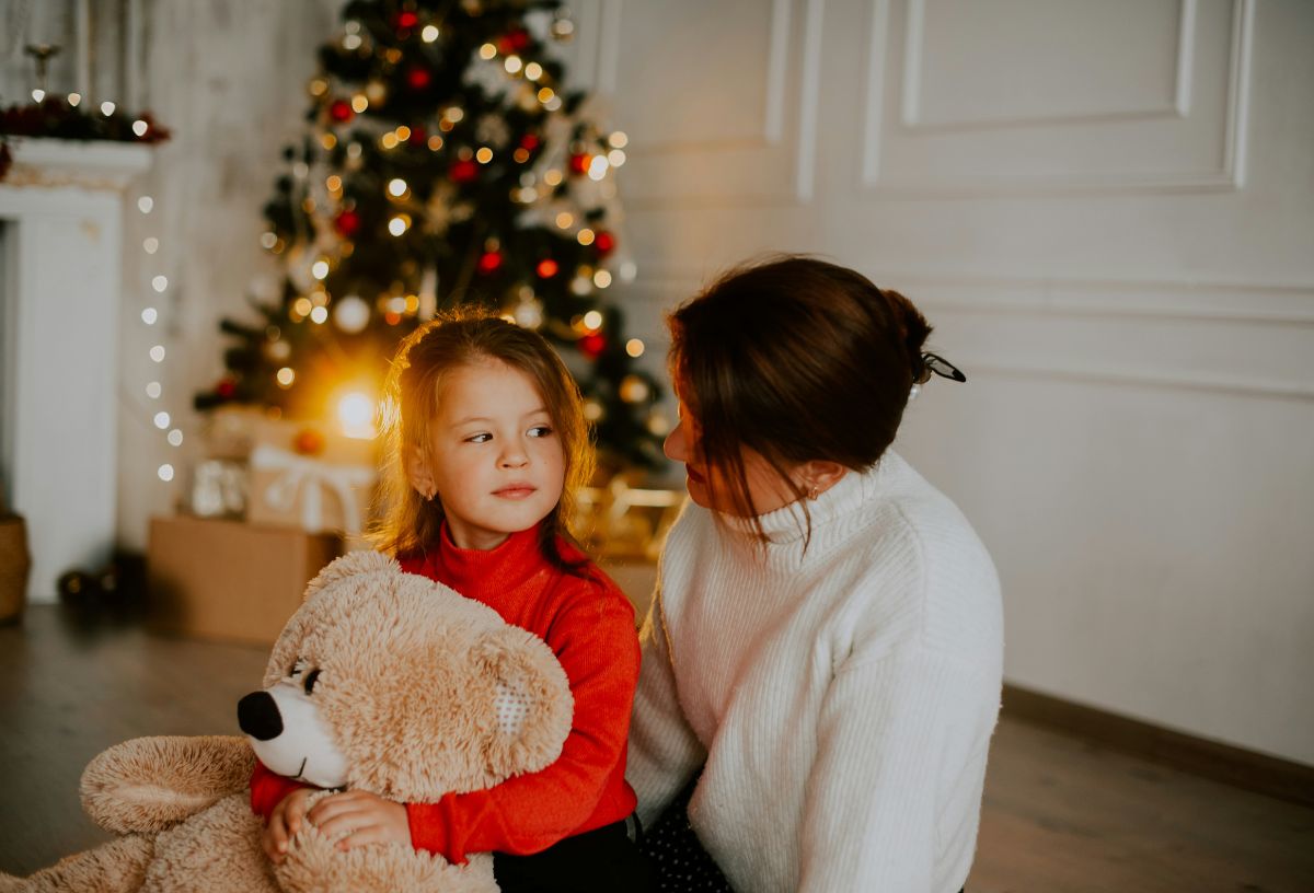 Anya és lánya karácsonyfa előtt beszélget, a lány kezében hatalmas plüssmackó