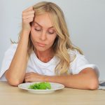 Szép szőke nő bámul unottan, undorodva egy salátalevelet a tányérján