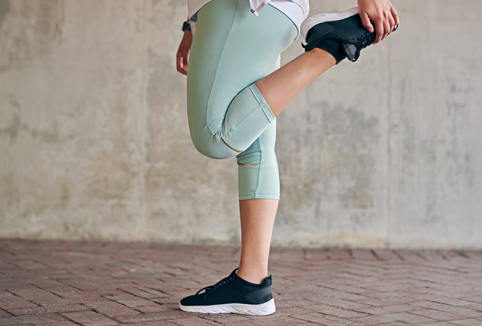 Közelkép egy sportos nőről, aki a szabadban edzés közben nyújtja a lábait.