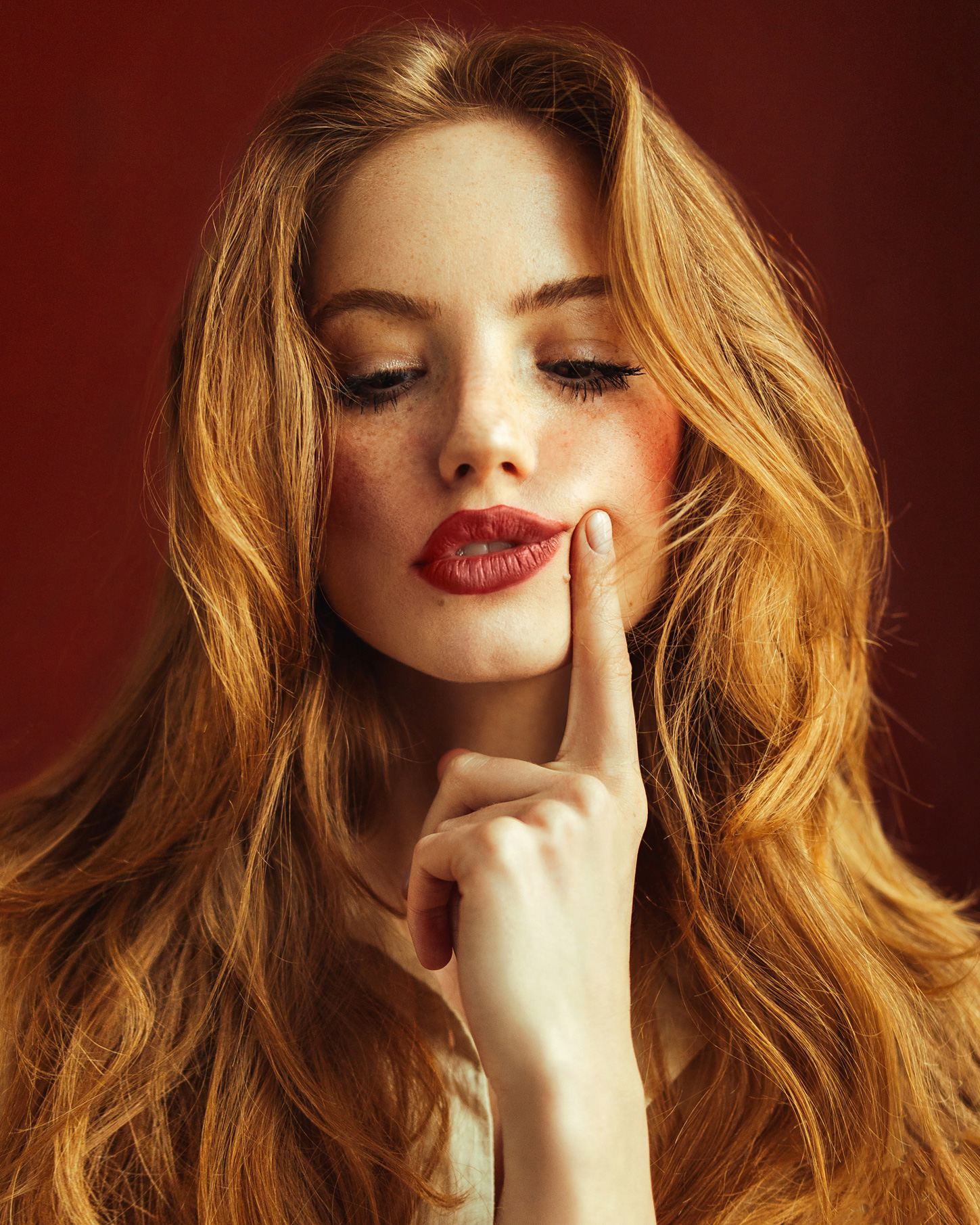 Egy vörös hajú, vörös rúzsos nő a mutató ujjával oldalra húzza a száját