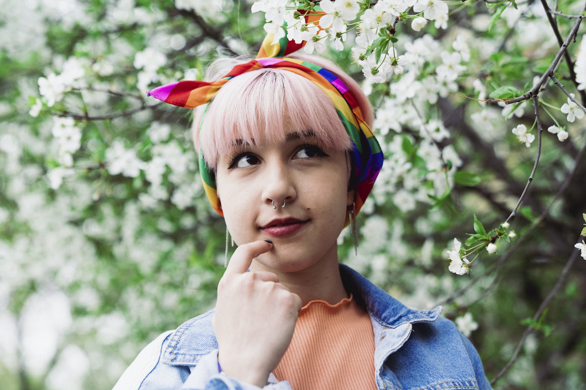 fiatal aktivista nő mosolyog, nyakában szivárványos sállal – az LMBTQ társadalmi mozgalom jelképével