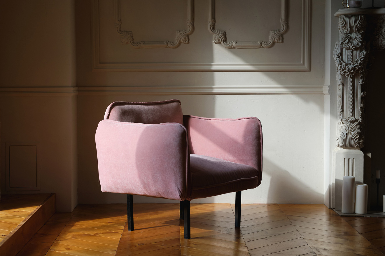 A nappali belső tere angol stílusú, rózsaszín velúr fotellel egy világos fal előtt. 