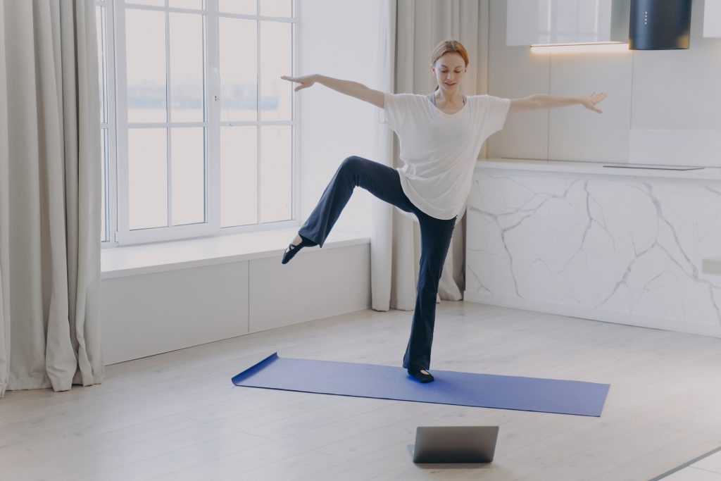 Fiatal nő fél lábon egyensúlyozik egy lila jógamatracon