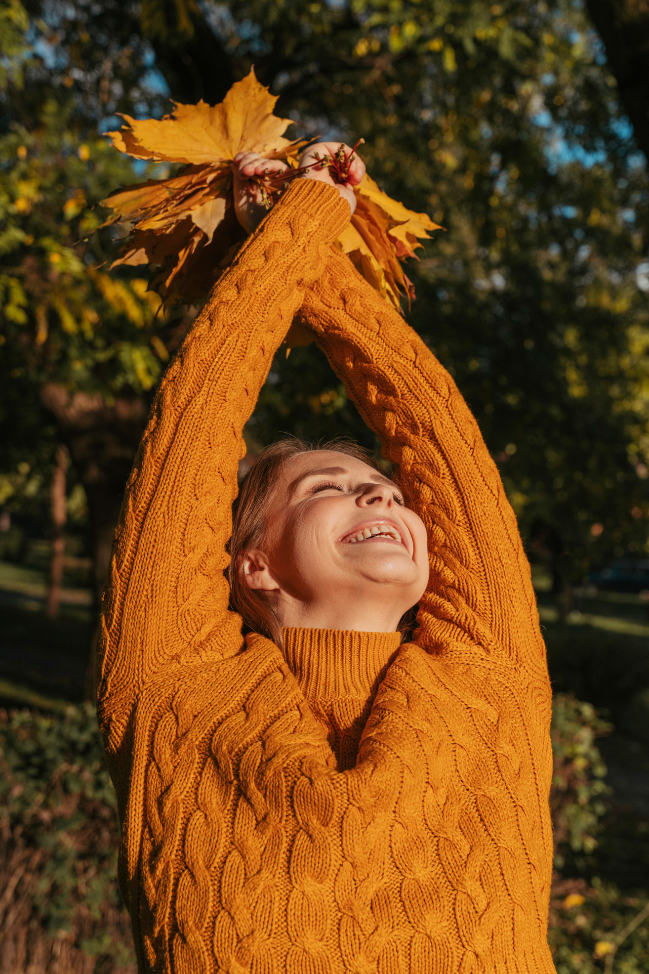 Vidám nő felemelt karokkal és juharlevélcsokorral a kezében egy őszi parkban