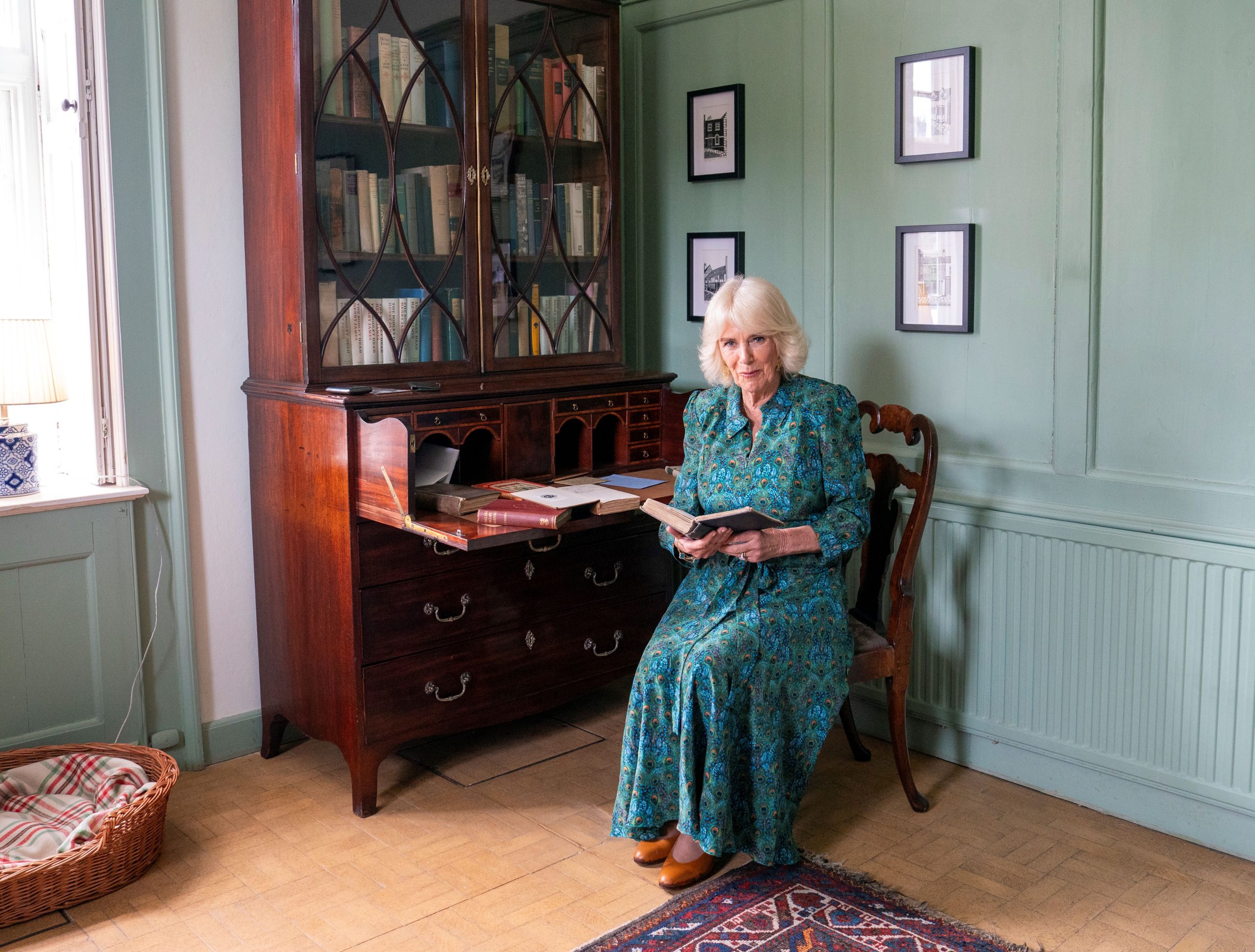 Kamilla királyné 2024. május 16-án az angliai Rye-ben, a Lamb House könyvtárában Henry James könyvének első kiadását nézi. Zöld ruhában ül egy széken közben.