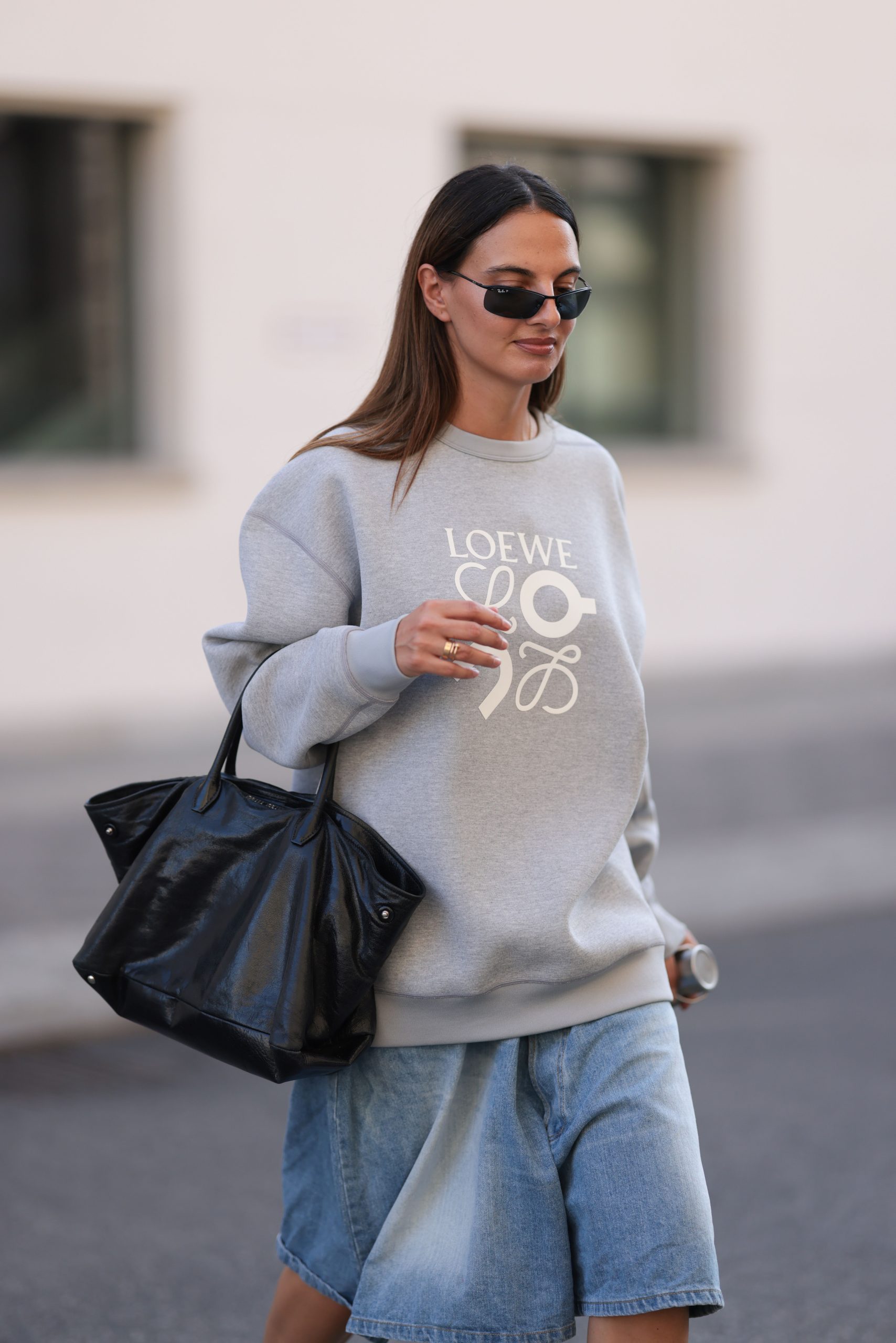 BArna hosszú hajú nő napszemüvegben, oversize pulóverben és nagy táskával a kezén