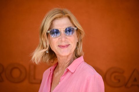 Michelle Laroque kék lencsés szemüvegben ls rózsaszín ingben, narancs háttér előtt