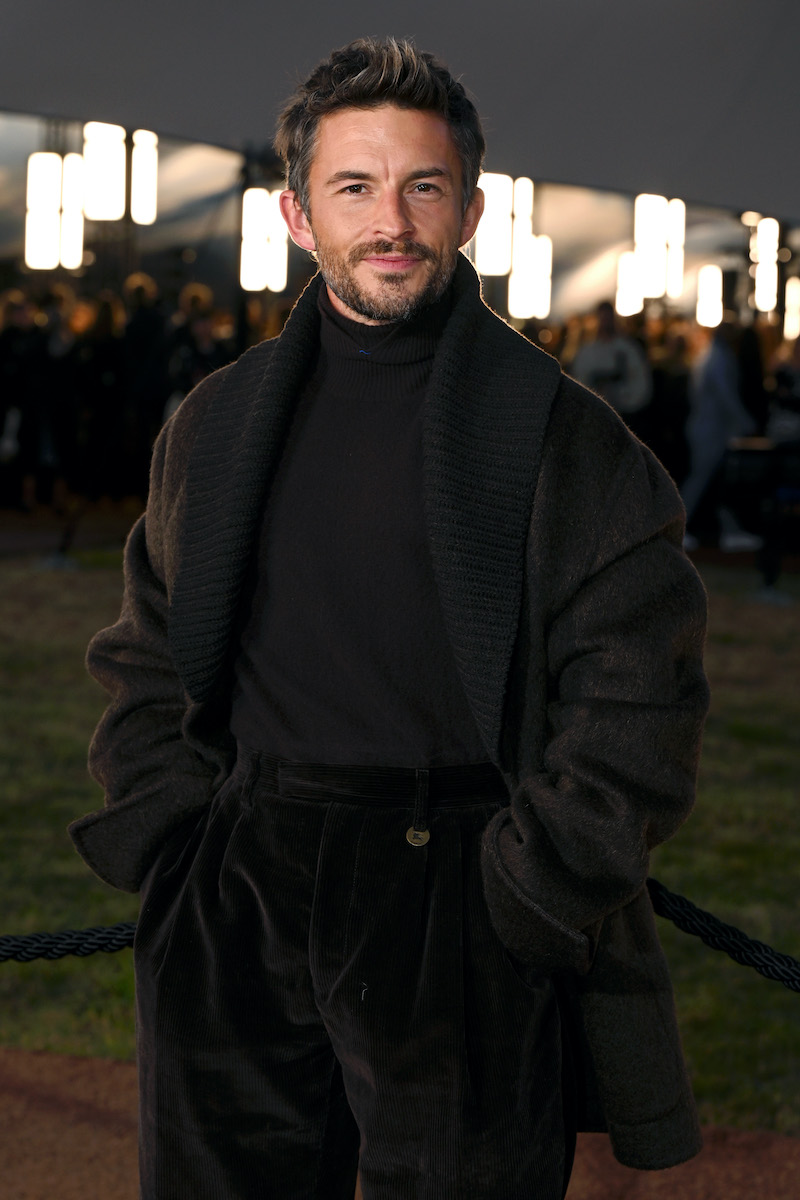 Jonathan Bailey barna szettben mosolyogva maga elé néz, a Burberry Summer 2026 showra érkezik – a London Fashion Week eseménye, 2025. szeptember 22.