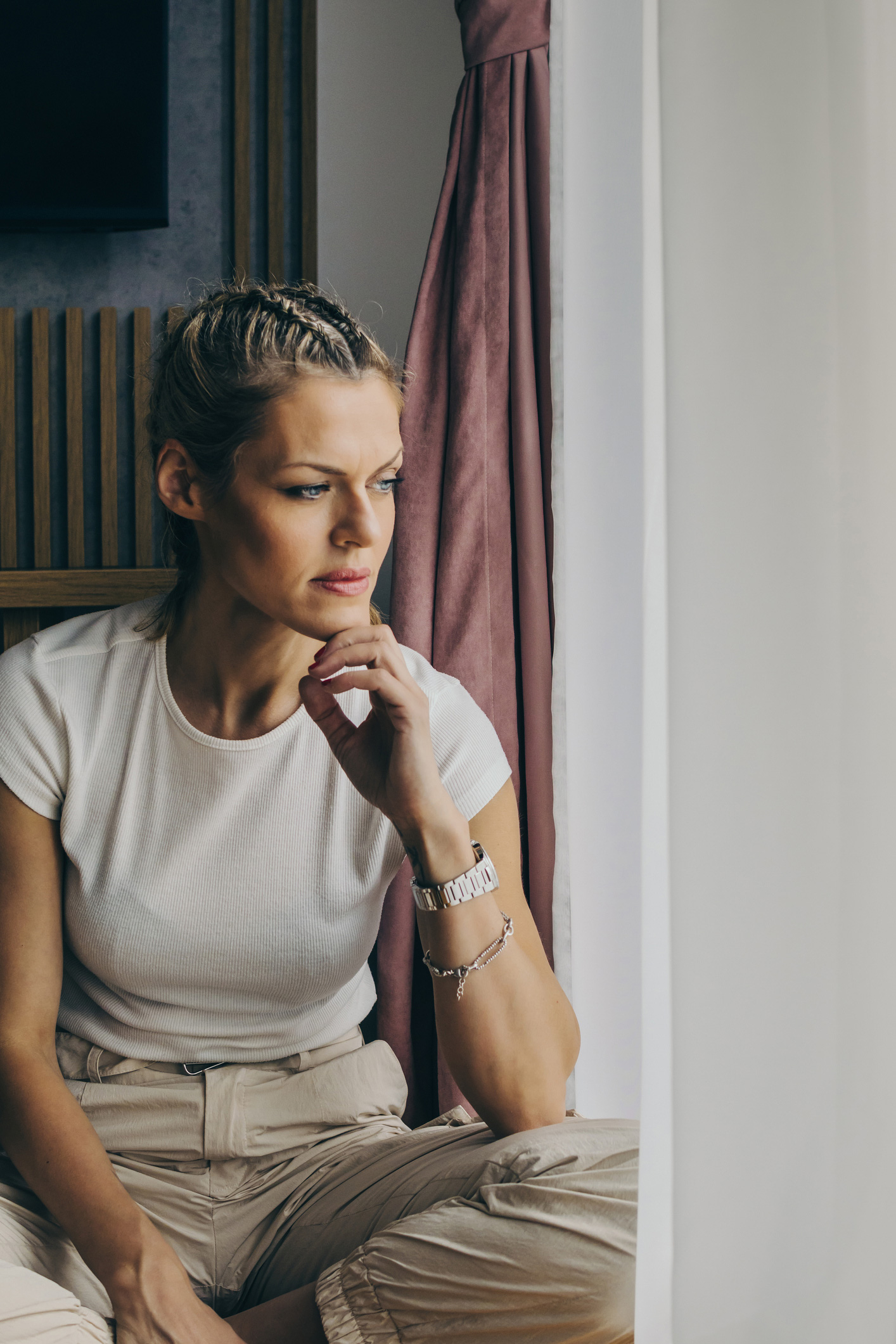 Depressziós, szorongó szőke nő, fonott hajával a padlón ül az ablak közelében