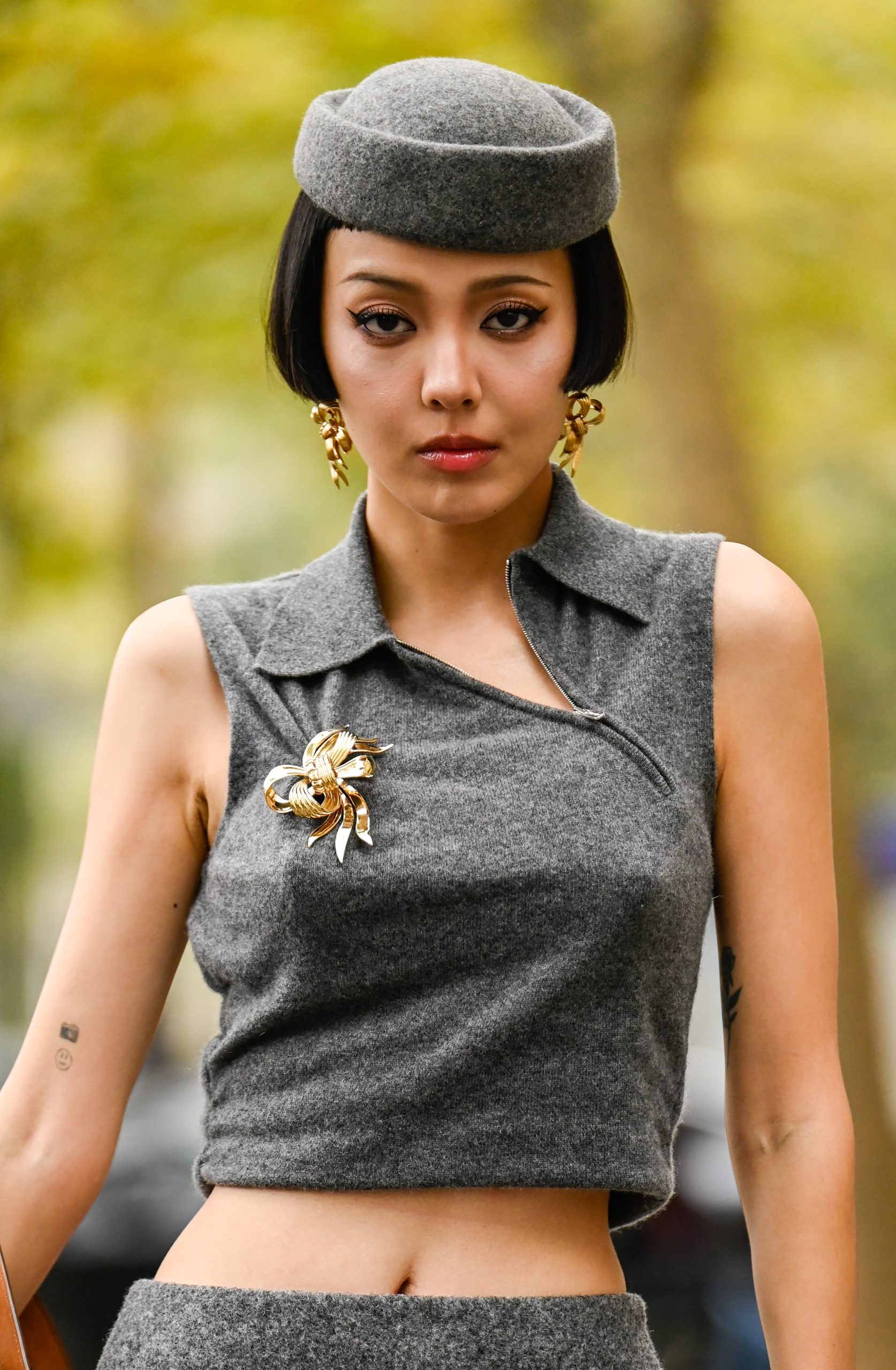 Barna hajú nő szürke kalapban és felsőben, arany brossal