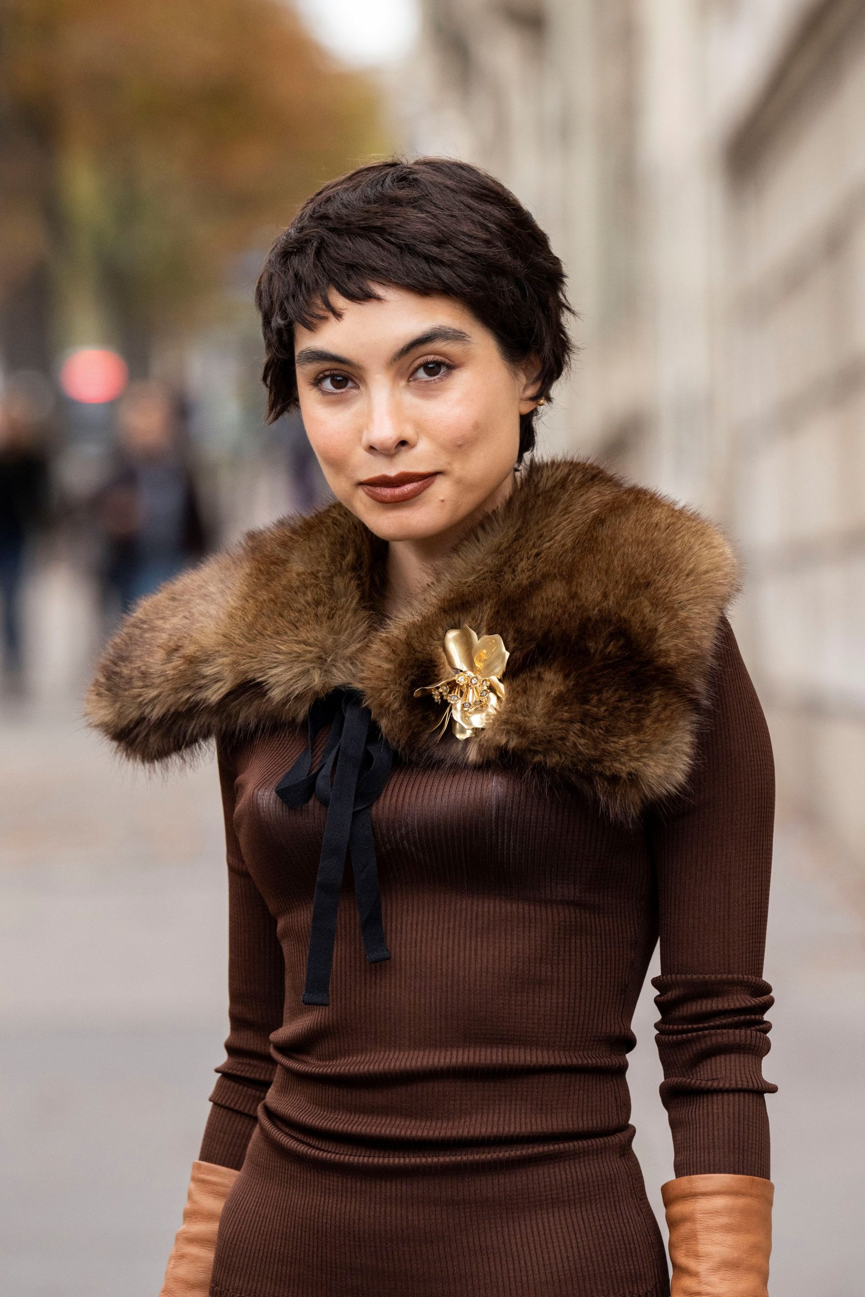 Barna hajú nő, barna ruhában arany brossal