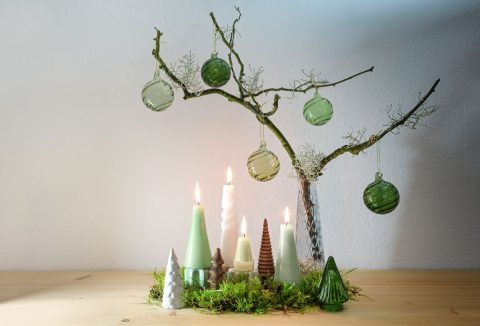 Rendhagyó adventi koszorú zöld árnyalatban, gallyakon zöldes üvegdíszek, fenyő alakú gyertyák a tövében