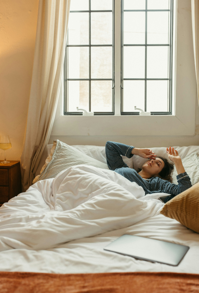 Nő ébredezik fehér ágyneműben, kék pizsamában